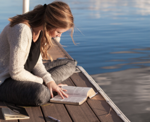 woman studying the Bible on the dock of a lake