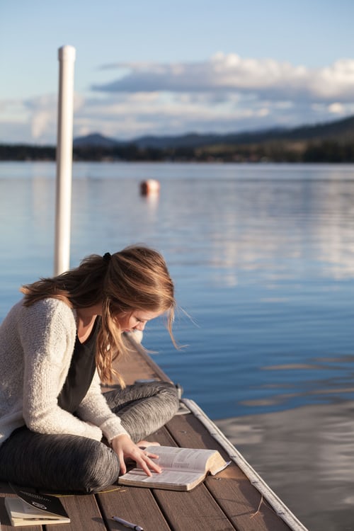 woman studying the Bible on the dock of a lake
